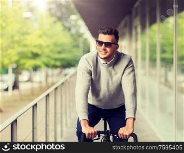 lifestyle, transport and people concept - happy smiling young man in sunglasses riding bicycle on city street. young man in shades riding bicycle on city street