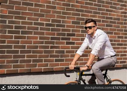 lifestyle, transport and people concept - young man in sunglasses riding bicycle on city street over brickwall