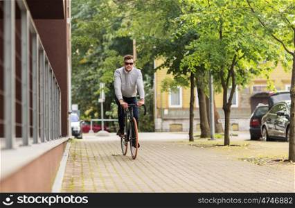 lifestyle, transport and people concept - young man in sunglasses riding bicycle on city street