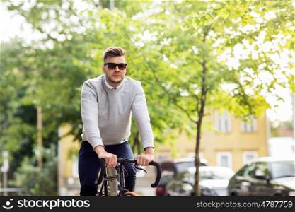 lifestyle, transport and people concept - young man in sunglasses riding bicycle on city street