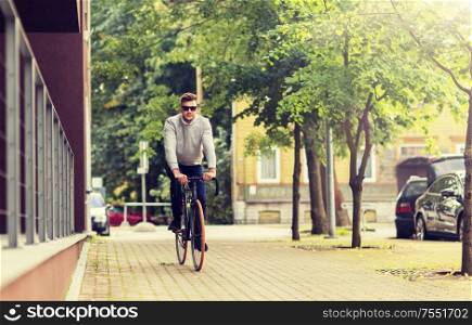lifestyle, transport and people concept - young man in sunglasses riding bicycle on city street. young man riding bicycle on city street