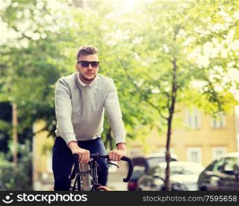 lifestyle, transport and people concept - young man in sunglasses riding bicycle on city street. young man in shades riding bicycle on city street