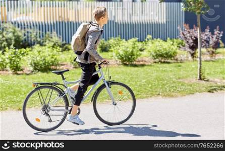 lifestyle, transport and people concept - young man or teenage boy with backpack riding bicycle on city street. young man riding bicycle on city street