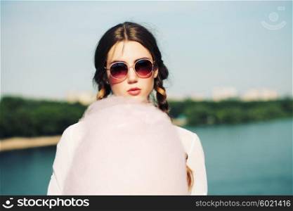 Lifestyle. Young happy hipster woman eating sweetened cotton candy, amazing view of the city from the bridge.