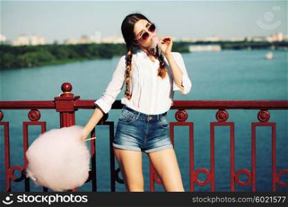 Lifestyle. Young happy hipster woman eating sweetened cotton candy, amazing view of the city from the bridge.