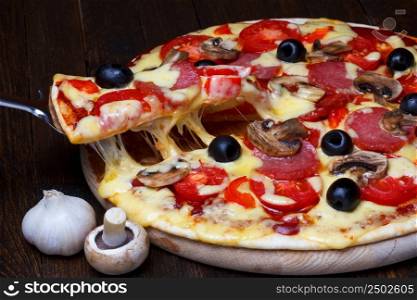 Lifted pizzza slice with melting cheese on dark wooden table