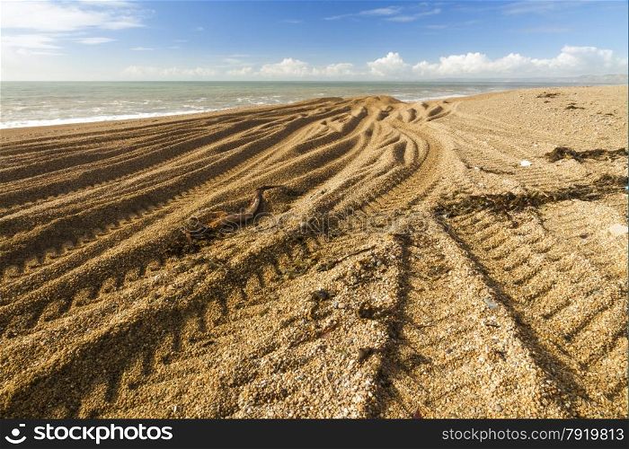 Light and shadow, beach made of pebbles with caterpillar tracks converging into distance.