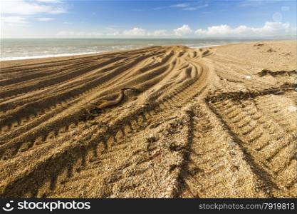 Light and shadow, beach made of pebbles with caterpillar tracks converging into distance.