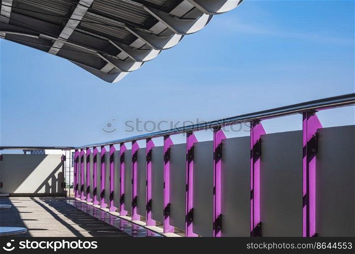 Light and shadow on surface of safety steel fence with roof on empty platform of the sky train station in downtown at Bangkok, Thailand against blue sky