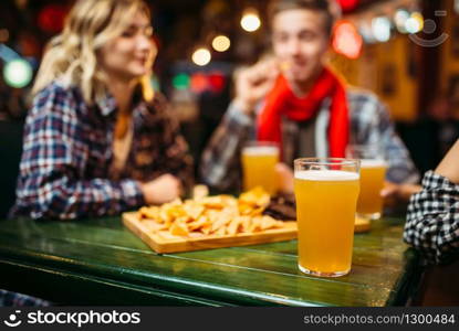 Light beer in glasses on the table in sports bar, football fans on background. Victory celebration, tv broadcasting, young friends leisures in pub