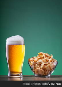 Light beer with foam in a glass and snacks in a transparent plate on a green background. Light beer with foam in glass and snacks in transparent plate on green background