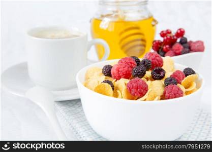 Light breakfast consisting of cornflakes with different berries, honey and cup of coffee