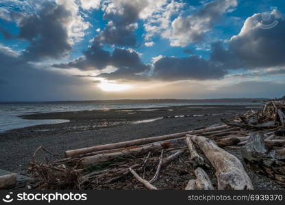 Light breaks through storm clouds onto a Puget Sound shoreline at low tide.