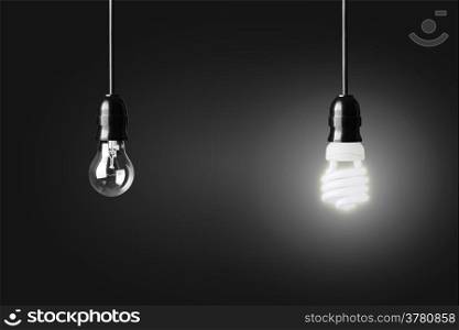 Light bulb and glowing energy saver bulb on black