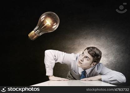 Light bulb concept. Young man leaning on table and looking at light bulb
