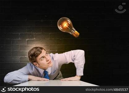 Light bulb concept. Young man leaning on table and looking at light bulb