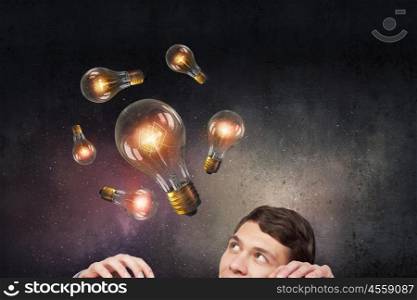 Light bulb concept. Young man looking from under table at glass light bulb
