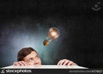 Light bulb concept. Young man looking from under table at glass light bulb