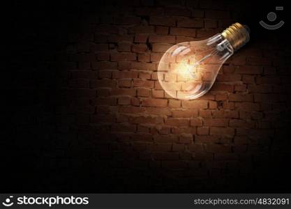 Light bulb on brick surface. Glass glowing light bulb on brick background