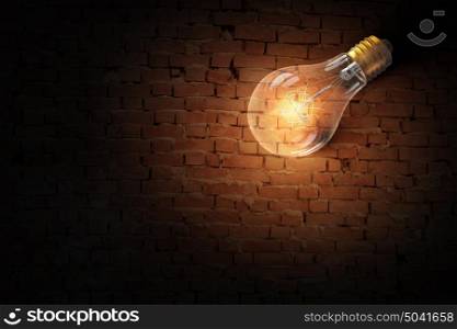 Light bulb on brick surface. Glass glowing light bulb on brick background