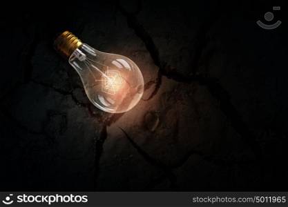 Light bulb on dry soil. Glass glowing light bulb on soil background