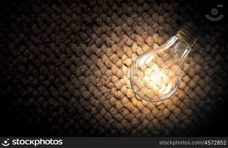 Light bulb on material surface. Power and energy concept with glass glowing light bulb o backdrop