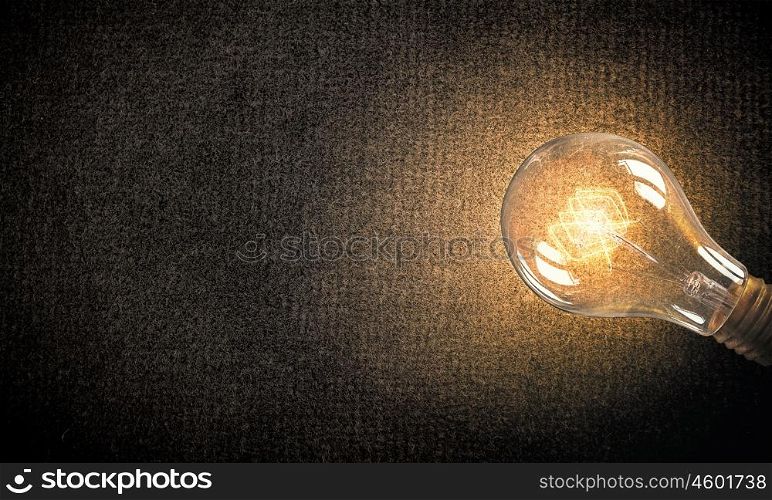 Light bulb on material surface. Power and energy concept with glass glowing light bulb o backdrop