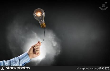 Light bulb on rope. Close up of hand holding glowing light bulb on rope