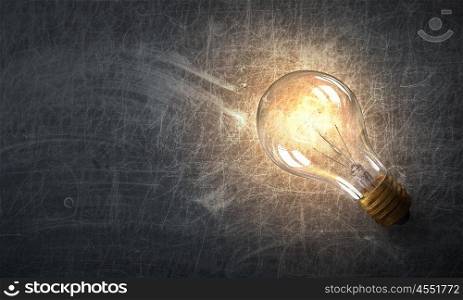 Light bulb on stone surface. Power and energy concept with glass glowing light bulb on concrete backdrop