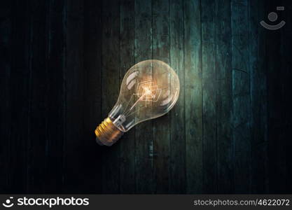 Light bulb on wooden surface. Glowing glass light bulb on wooden background