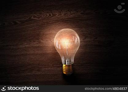 Light bulb on wooden surface. Glowing glass light bulb on wooden background