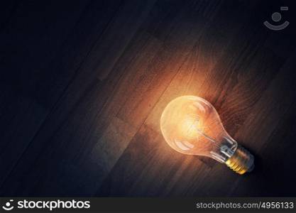 Light bulb on wooden surface. Glowing glass light bulb on wooden background