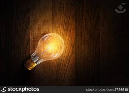 Light bulb on wooden surface. Glowing glass light bulb on wooden table