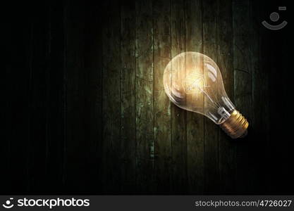 Light bulb on wooden surface. Glowing glass light bulb on wooden table