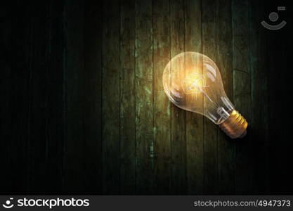 Light bulb on wooden surface. Glowing glass light bulb on wooden table