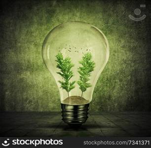 Light bulb with soil, green trees growing inside and birds flying. Energy conservation and environmental friendly concept. Green shining lamp on gray background.
