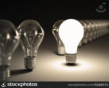Light bulbs in a row with glowing one on black background.