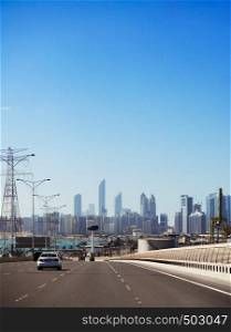 Light Cars Traffic on highway overpass to Abu Dhabi city center with skyscraper buildings under blue summer sky