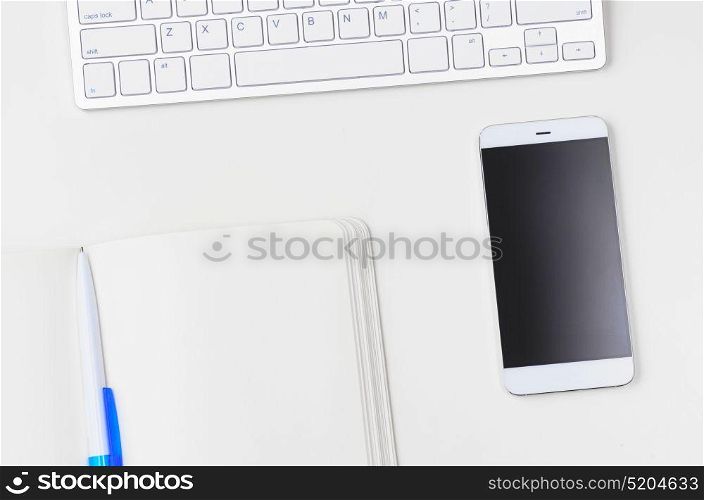 Light clean workplace. White workplace with keyboard, smartphone and notebook, view from above