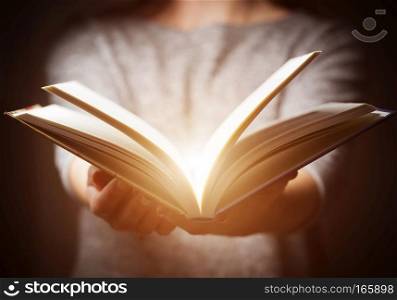 Light coming from book in woman?s hands in gesture of giving, offering. Concept of wisdom, religion, reading, imagination.. Light coming from book in woman?s hands in gesture of giving