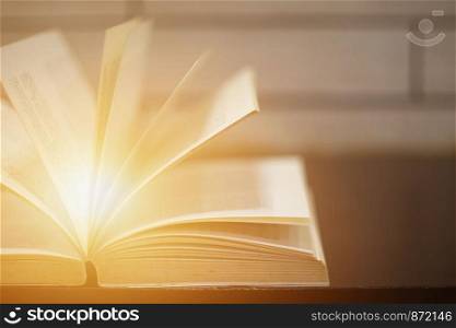 Light coming from open book on the desk over wooden background. Education learning concept.