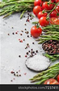 Light food background with healthy organic cherry tomatoes, asparagus and rosemary with bowl of pepper and salt. Vertical
