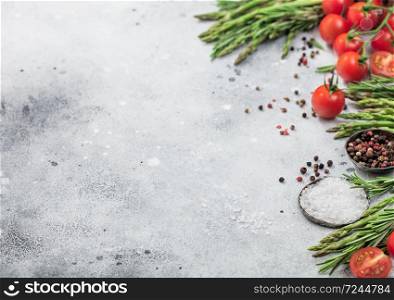 Light food background with healthy organic cherry tomatoes, asparagus and rosemary with bowl of pepper and salt. Space for text