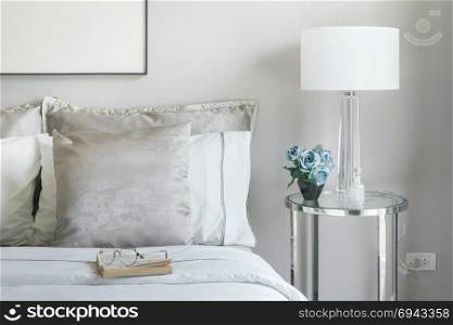 Light gray and white pillows on bed with flower jar on bedside table