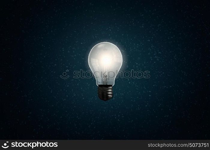 Light in darkness. Glass glowing light bulb on dark background