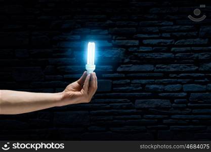 Light in darkness. Human hand on dark background holding glass light bulb