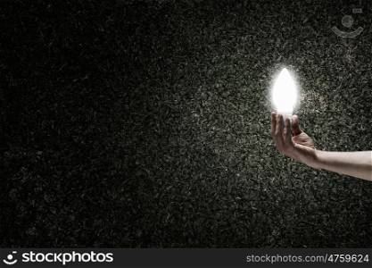Light in darkness. Human hand on dark background holding glass light bulb