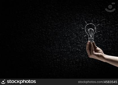 Light in darkness. Human hand on dark background holding light bulb