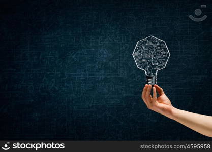 Light in darkness. Human hand on dark background holding light bulb