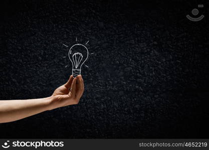 Light in darkness. Human hand on dark background holding light bulb